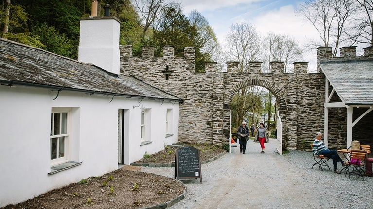 White single storey building with large chimneys and courtyard with castellated archway in the background